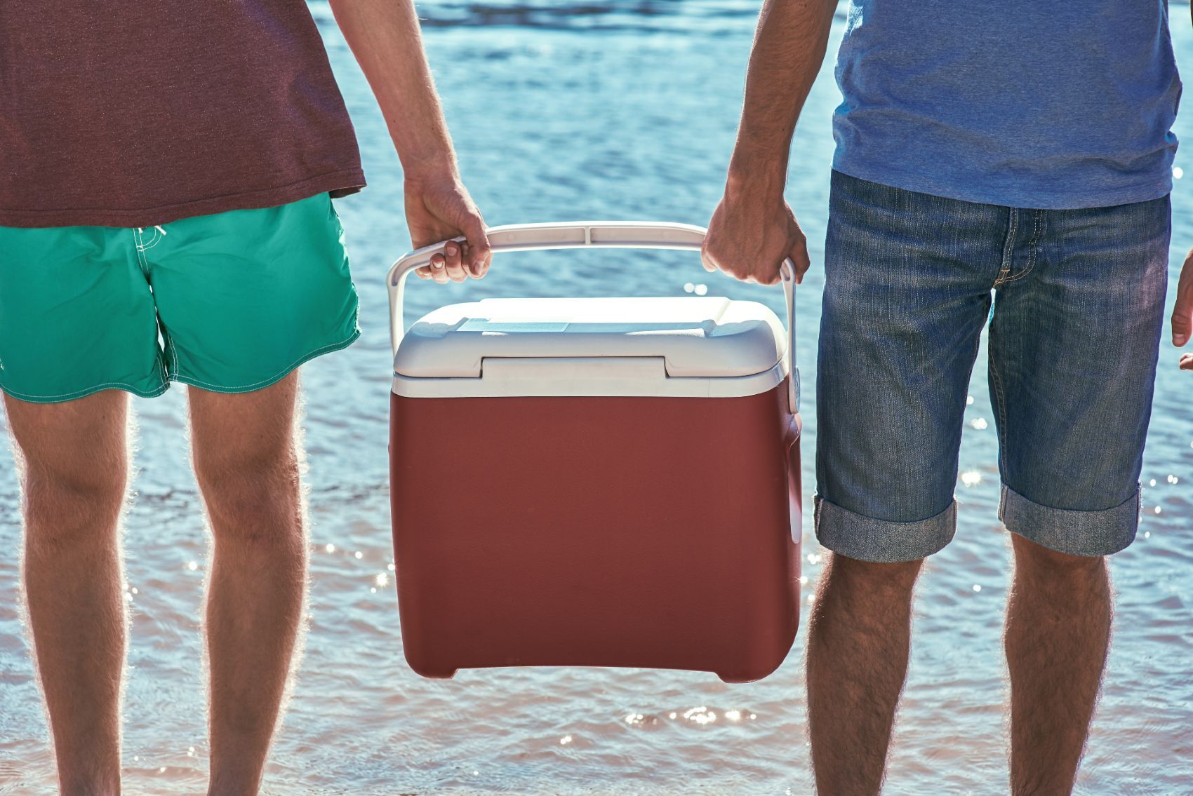 Two men carry a red cooler between them near the water - coleman ice cooler