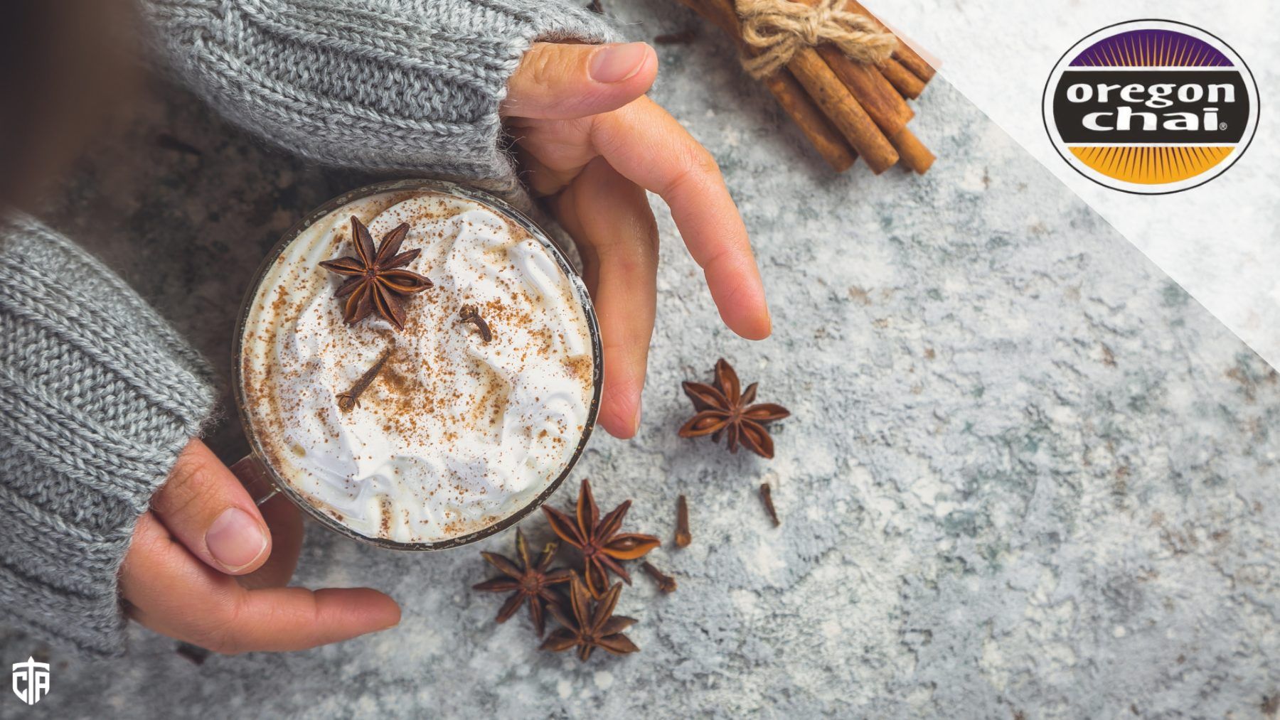 A person holds their hands around a chai latte in a cup, surrounded by spices - chai tea latte
