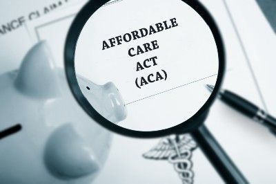 Affordable Care Act paperwork under a magnifying glass near a pen and piggy bank