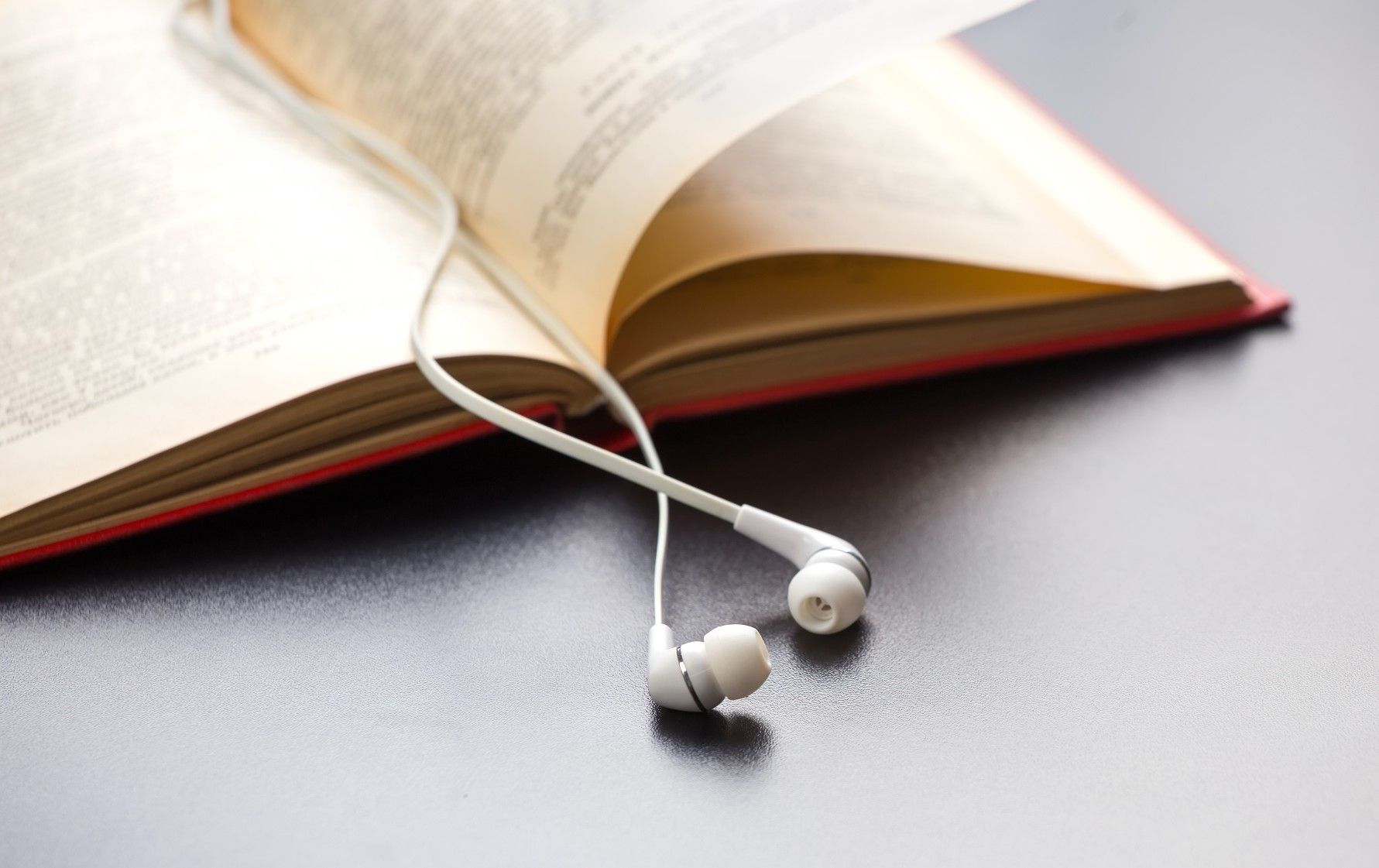 A set of white earbuds lie across an open book - Audible free trial