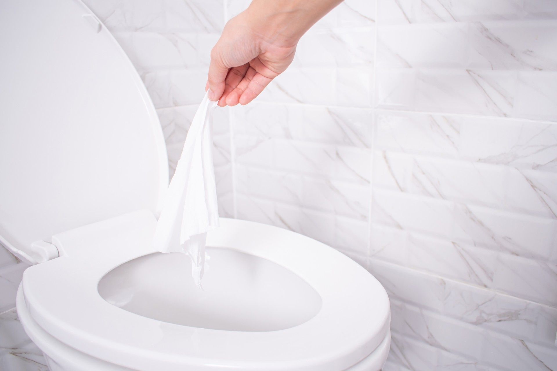 A person throws a wipe into a toilet near a white marble wall - flushable wipes