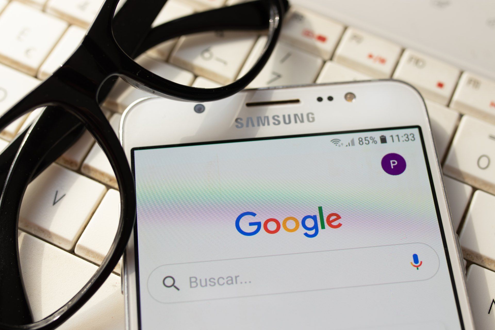 A Samsung smartphone with Google on the screen sits with glasses on top of a keyboard - Google tracking