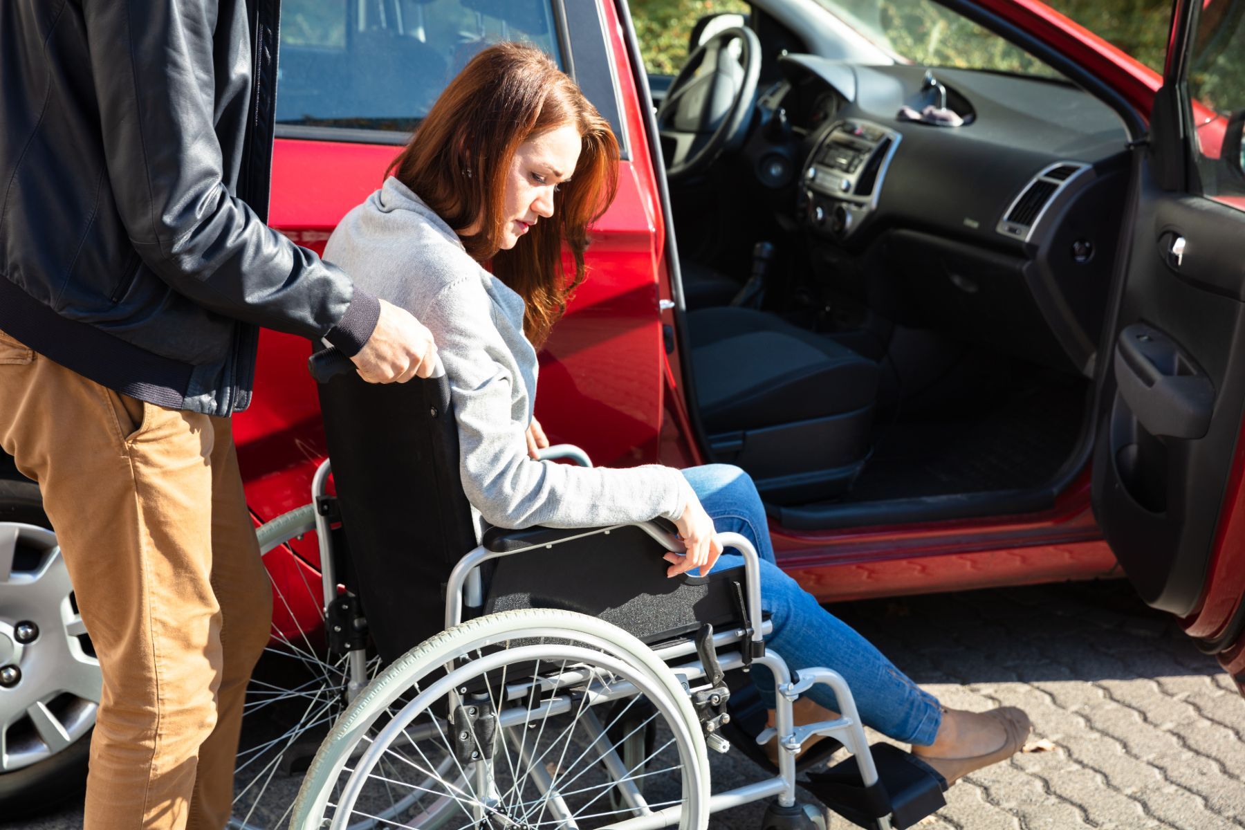 A man pushes a woman in a wheelchair up to the open passenger-side door of a red vehicle - Lyft wheelchair accessibility