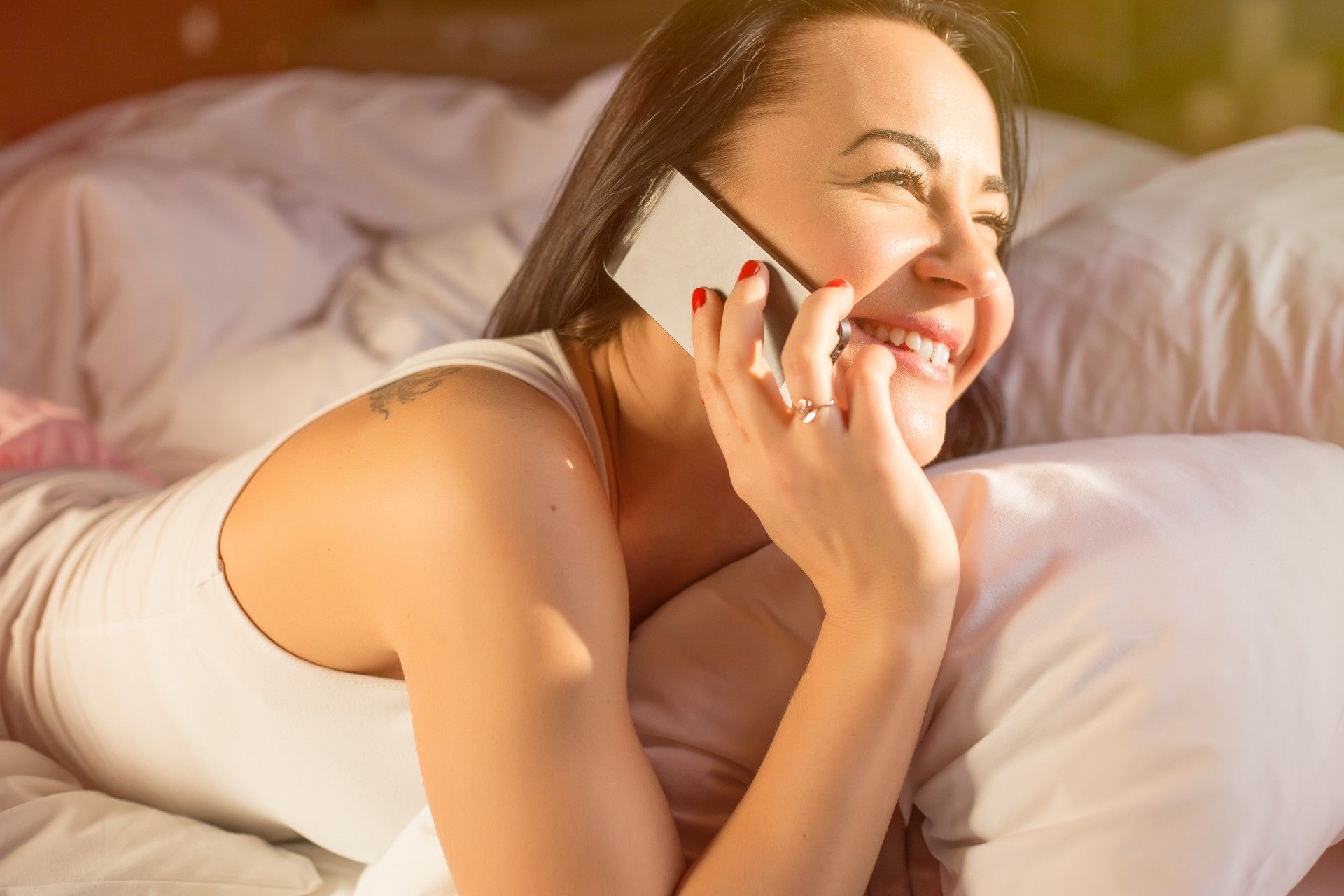 A smiling woman talks on an iPhone while lying on her stomach in bed - iPhone radiation