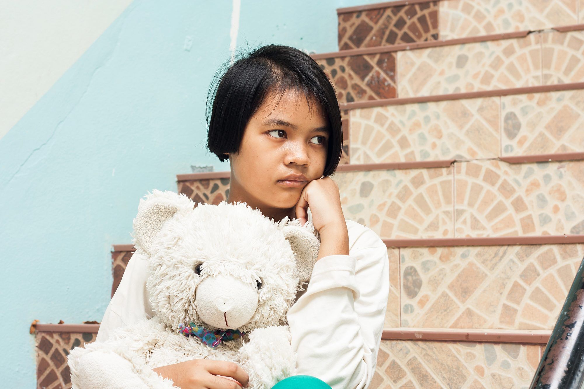 Girl holding teddy bear sits on steps