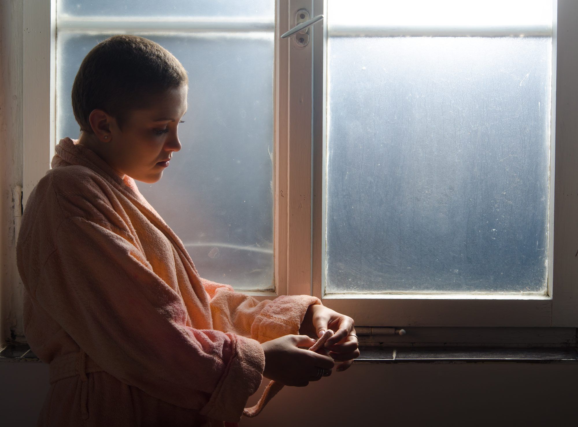 Young woman cancer survivor next to window