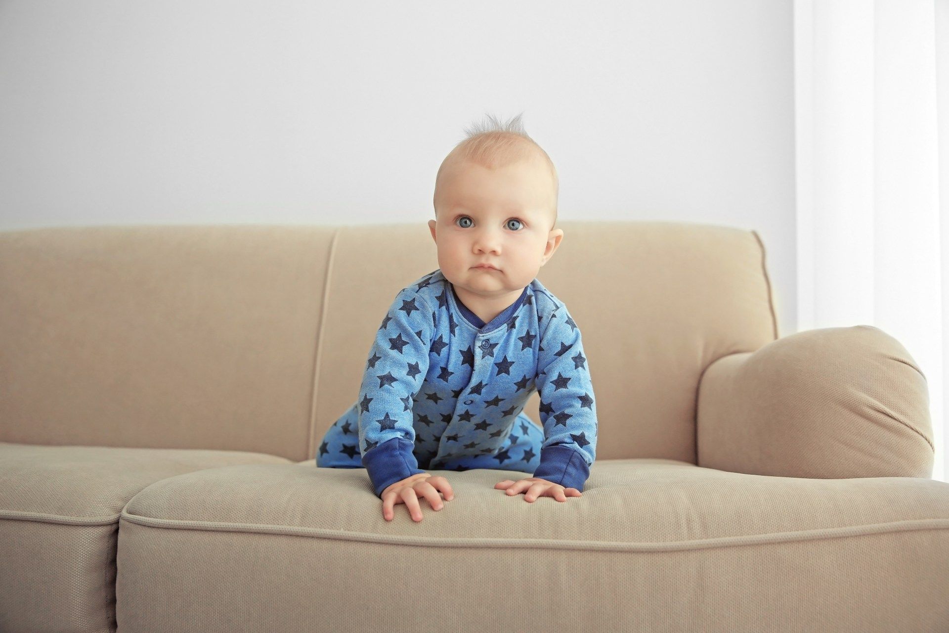 A baby wearing a blue romper crawls on a tan sofa - target recalls