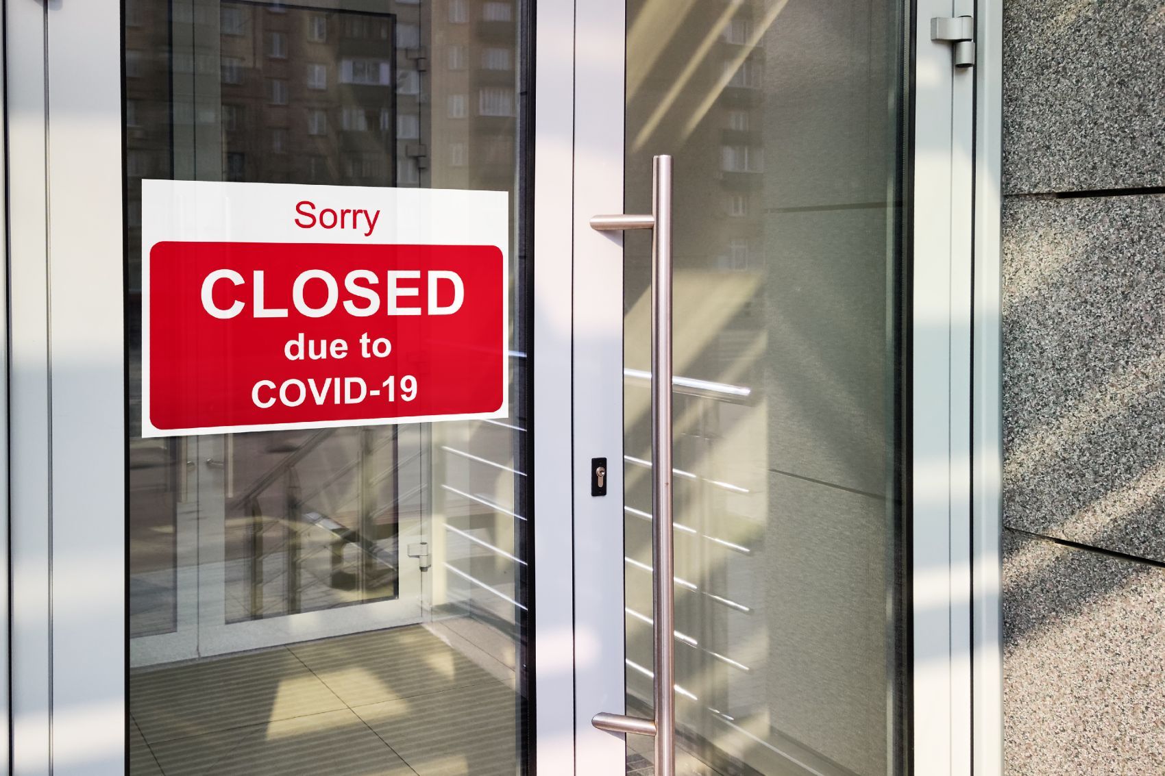 A red-and-white sign on the glass door of a business reads "Sorry CLOSED due to COVID-19" - coronavirus restrictions