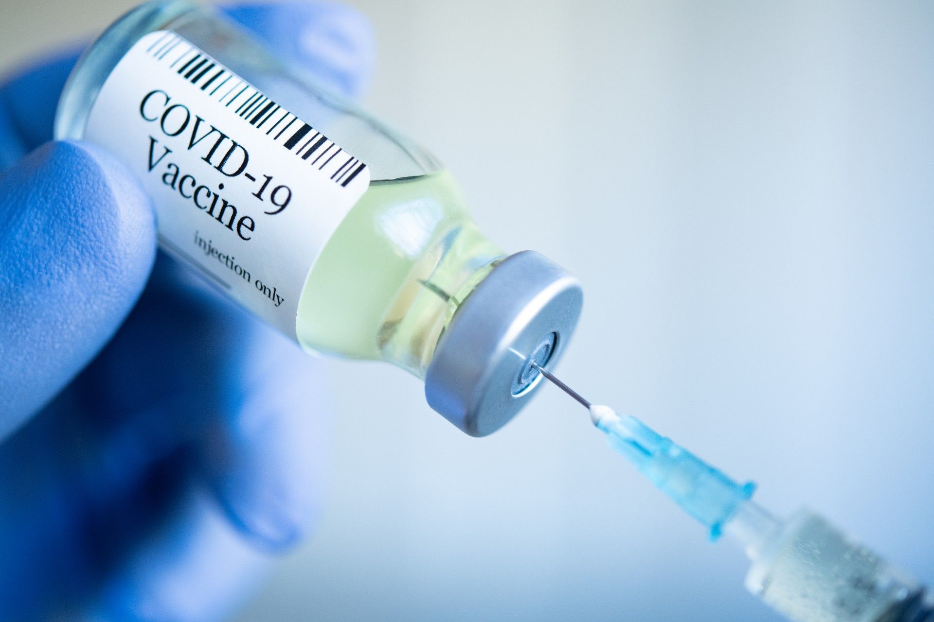 A person wearing blue gloves fills a syringe from a vial that reads "COVID-19 vaccine" - coronavirus vaccine