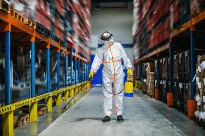 A person in a hazmat suit disinfects a warehouse - worker safety