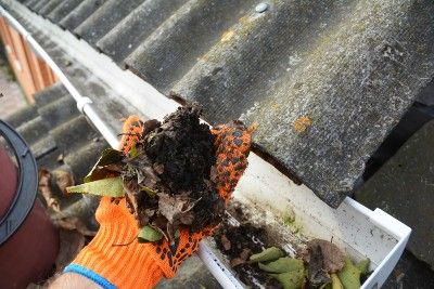 An orange-gloved hand holds debris pulled from gutter - LeafFilter gutter system