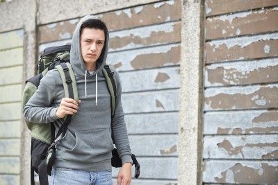 A homeless young man in a hoodie with a rucksack on his back - homeless youth