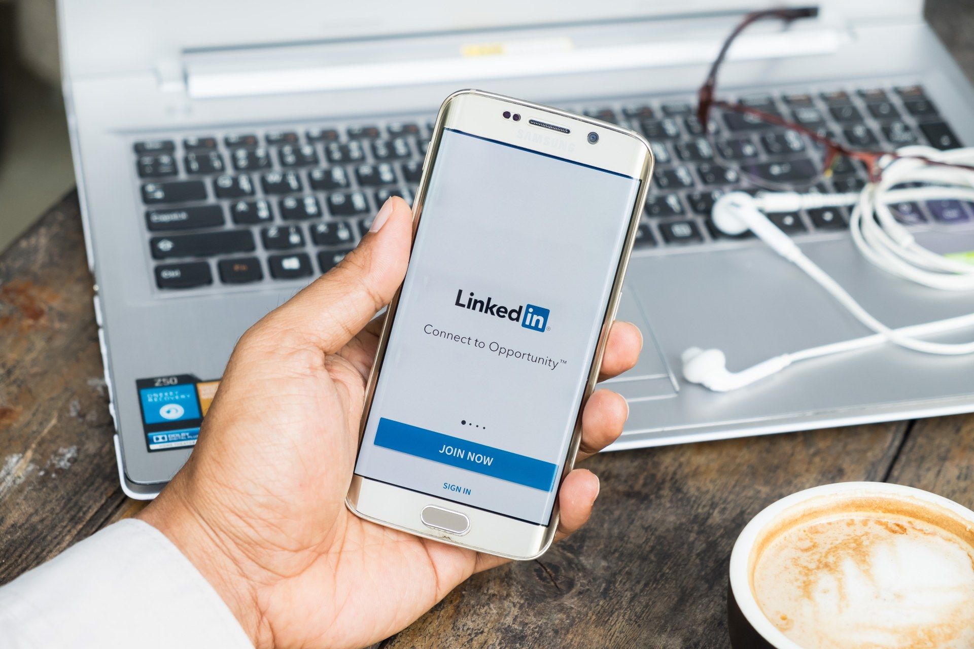 A man uses LinkedIn on his phone with his laptop sitting open in front of him - LinkedIn ads