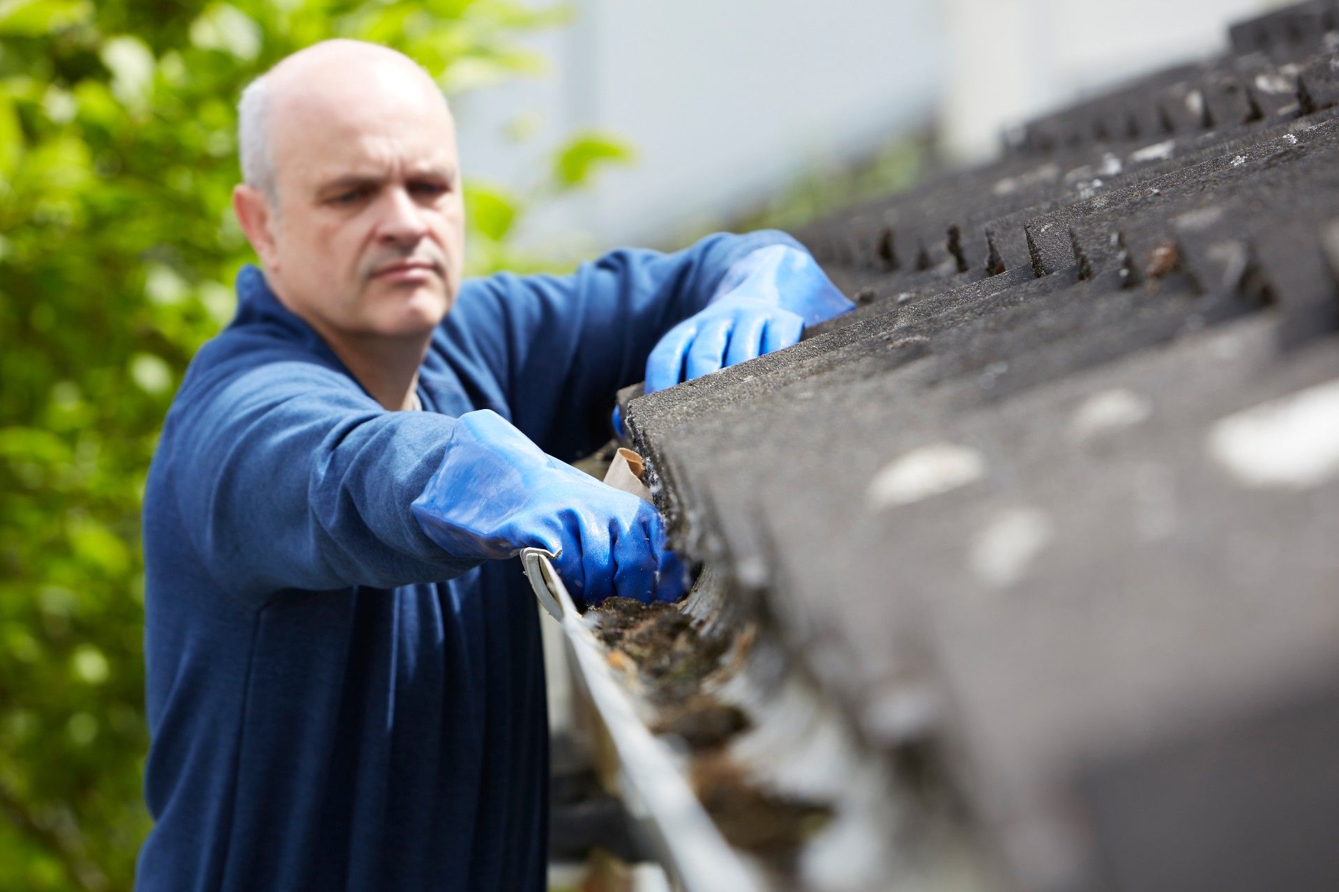 A man in blue gloves cleans the gutter on a house - LeafFilter gutter system
