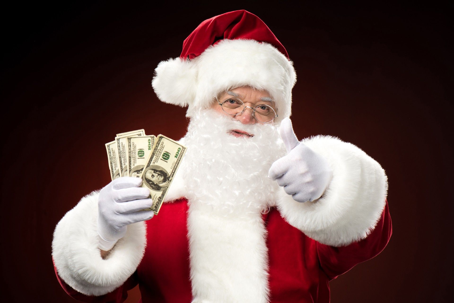 Santa Claus holds money in one hand and gives a thumbs up with the other - checks in the mail