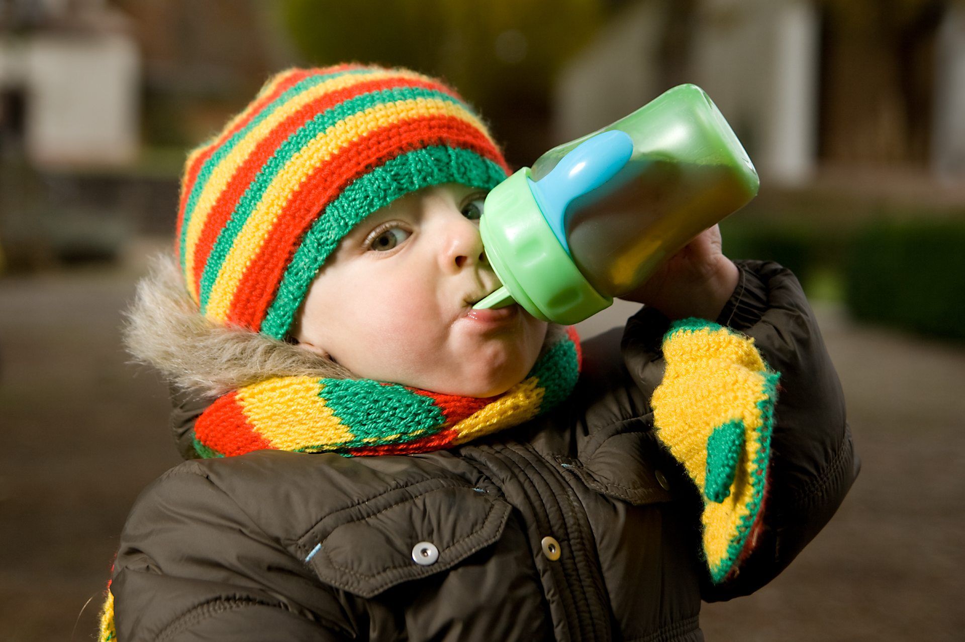 A toddler in a winter coat and colorful cap drinks from a sippy cup - Similac Go & Grow Toddler Drink