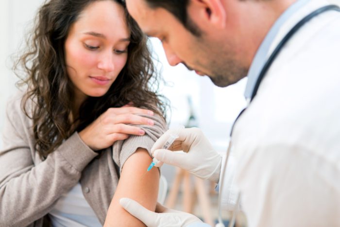 A doctor vaccinates a young woman with dark hair