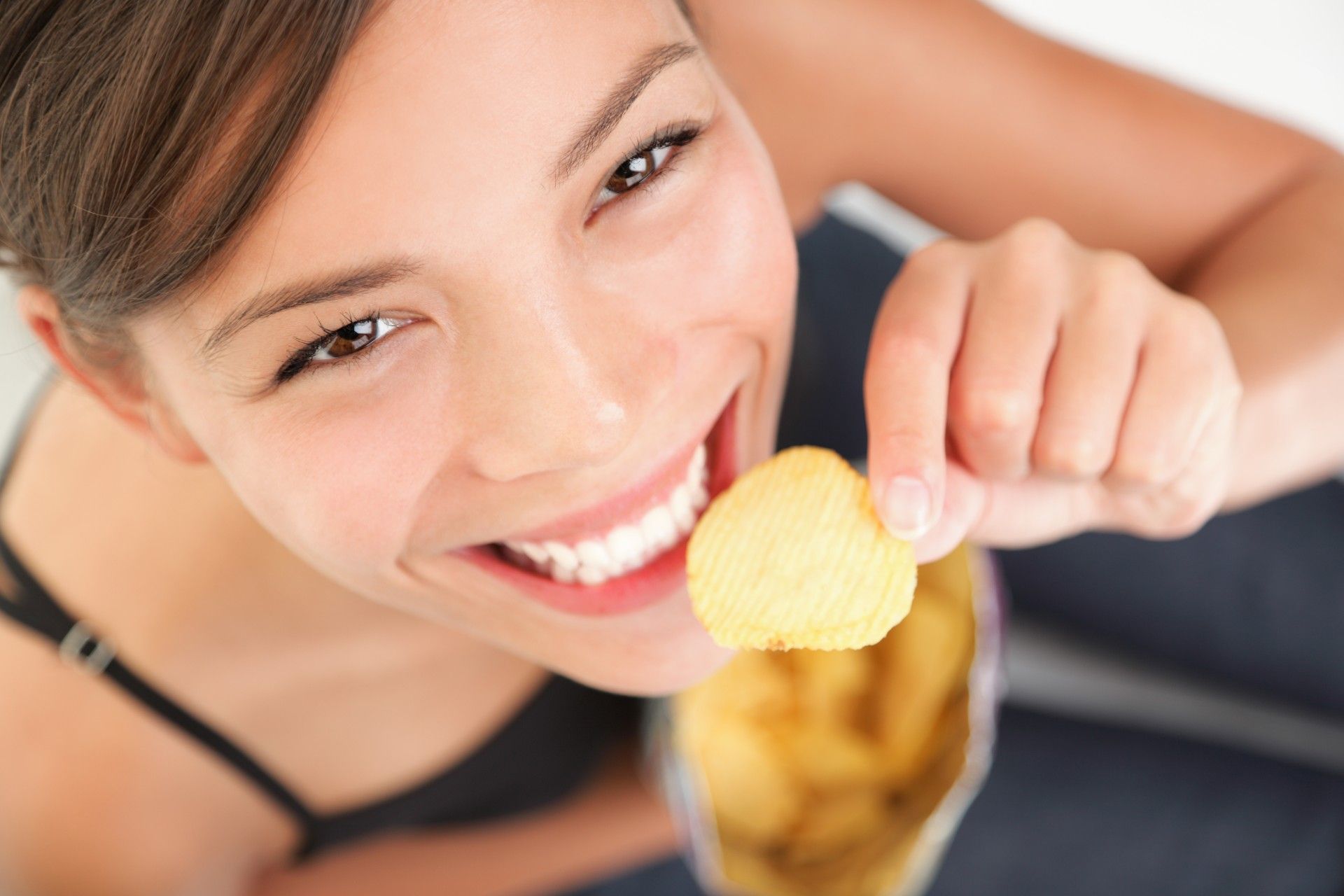 A woman looks up at the camera while eating chips - artificial flavors