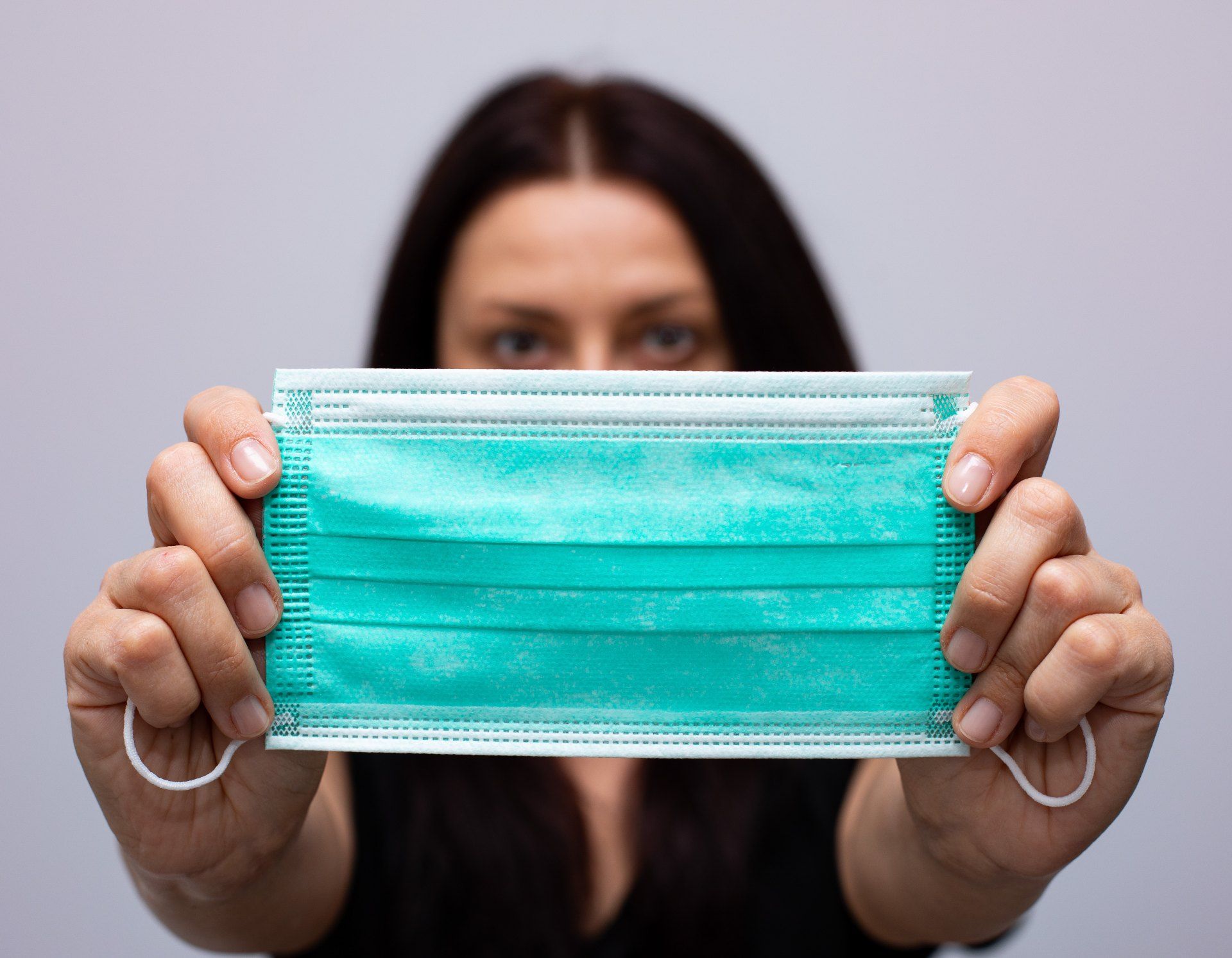 A woman holds out a blue-green surgical mask using both hands - sales tax