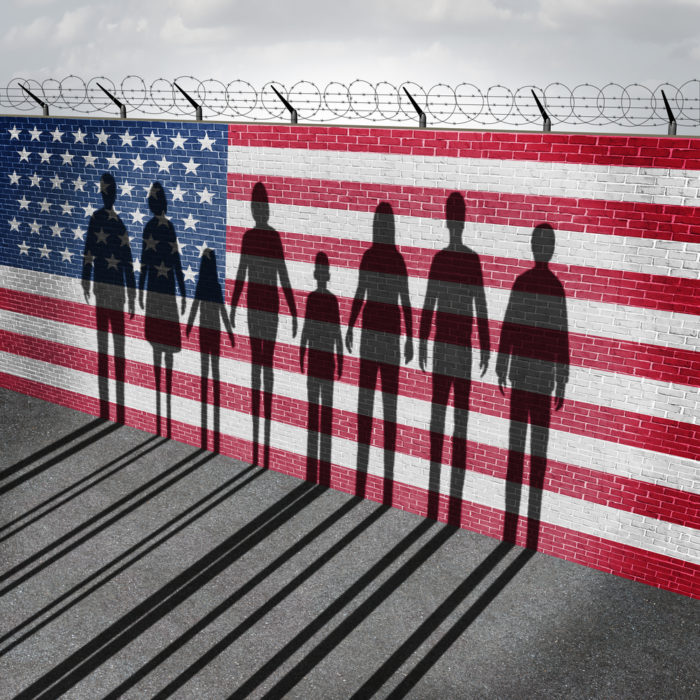 Silhousettes of people against a wall painted like the U.S. flag with concertina wire on top - libre by nexus
