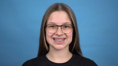 A girl with braces and glasses smiles at the camera