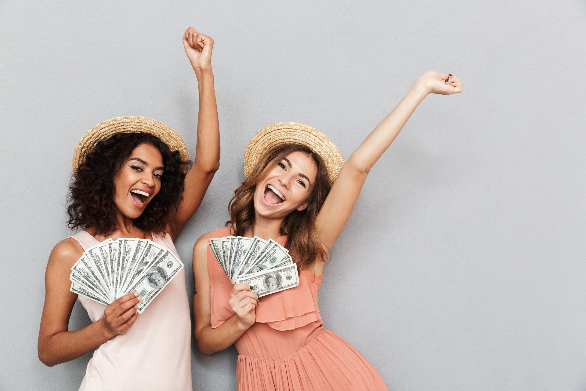 Two women celebrate while holding up fanned-out cash - settlement payout