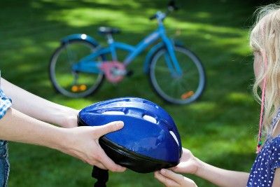 A person hands a child a blue bike helment outdoors - Trek Bicycle helmet