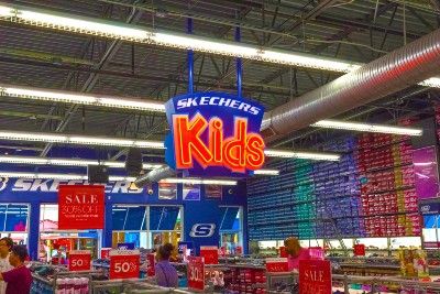 A Skechers Kids sign hangs from the ceiling of a Skechers store - Skechers light-up shoes