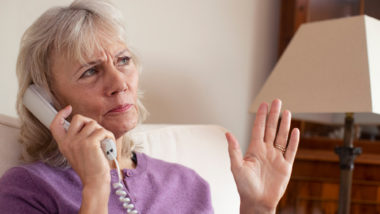 A senior woman in a purple shirt gestures as she talks on a landline phone - yodel technologies