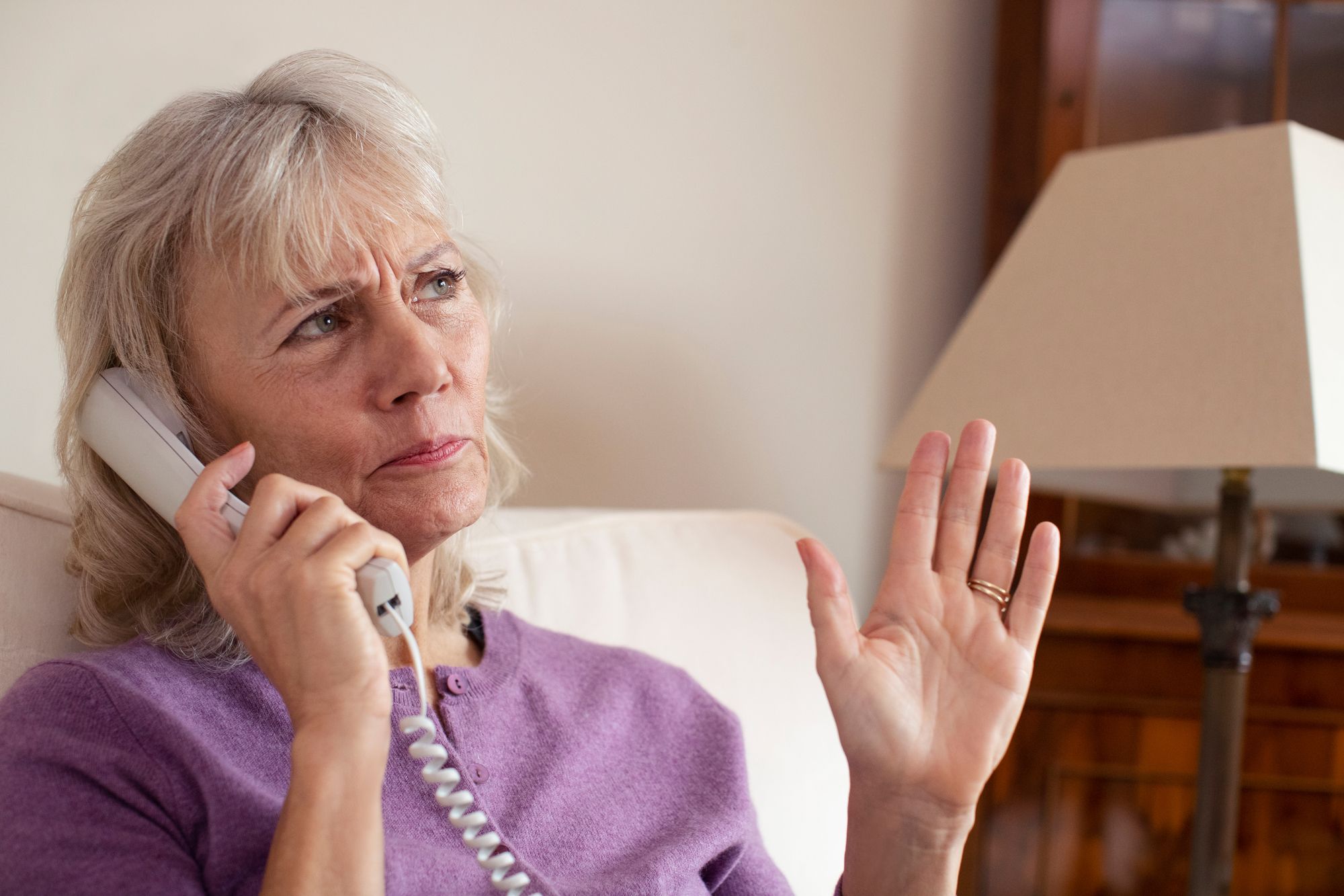 A senior woman in a purple shirt gestures as she talks on a landline phone - yodel technologies