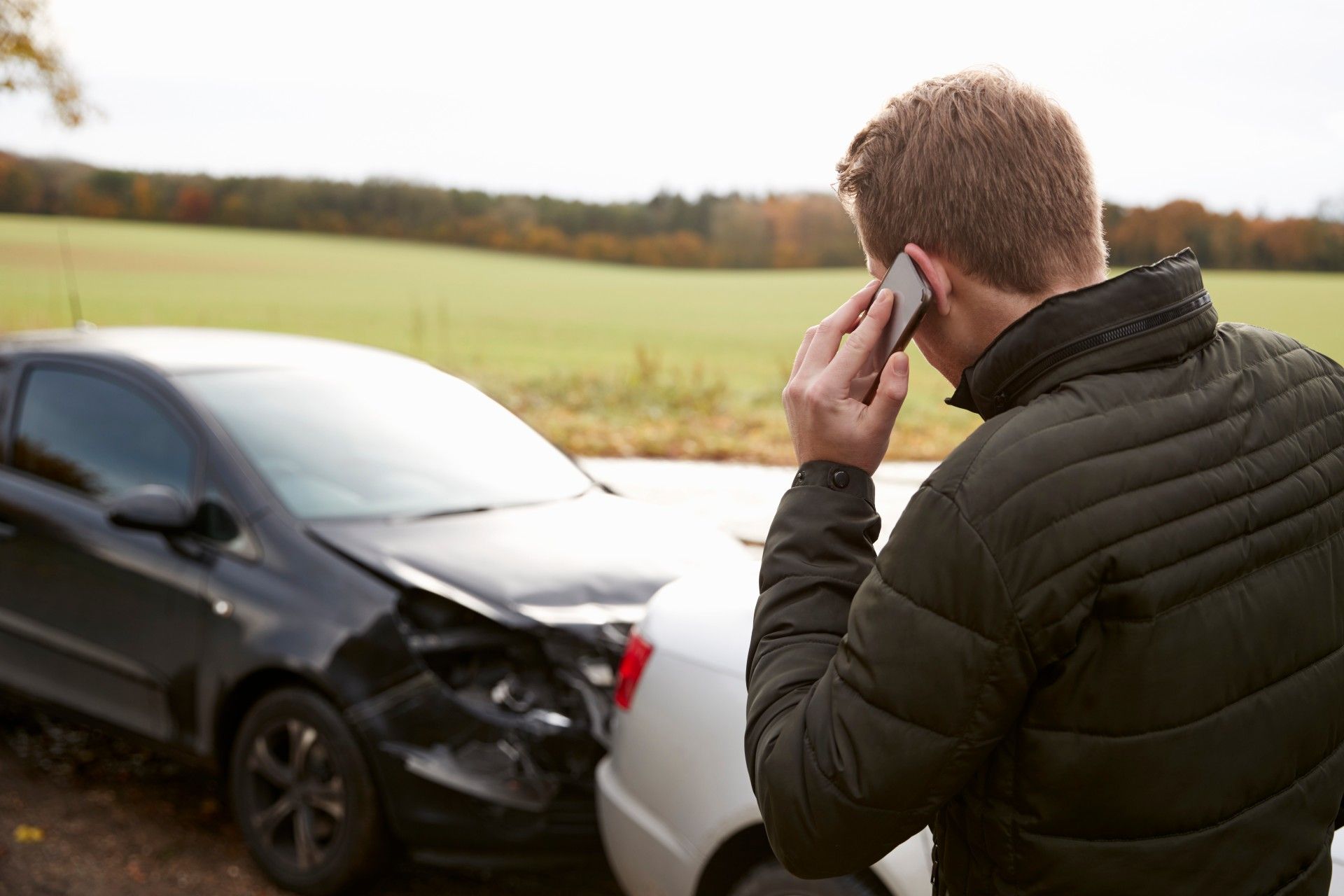 A man talks on his cellphone while standing near the scene of a car accident - crash reports