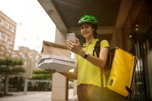 A smiling woman food courier wears a bike helmet and looks at her phone - food delivery