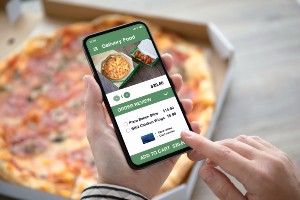 A person with a pizza looks at a food delivery app on their smartphone 