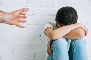 A man's hand reaches for a child who is resting their head on their arms on top of their knees - sexual assault