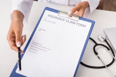 A doctor hands a pen and a clipboard with an insurance claim form to someone off-camera - bcbs settlement