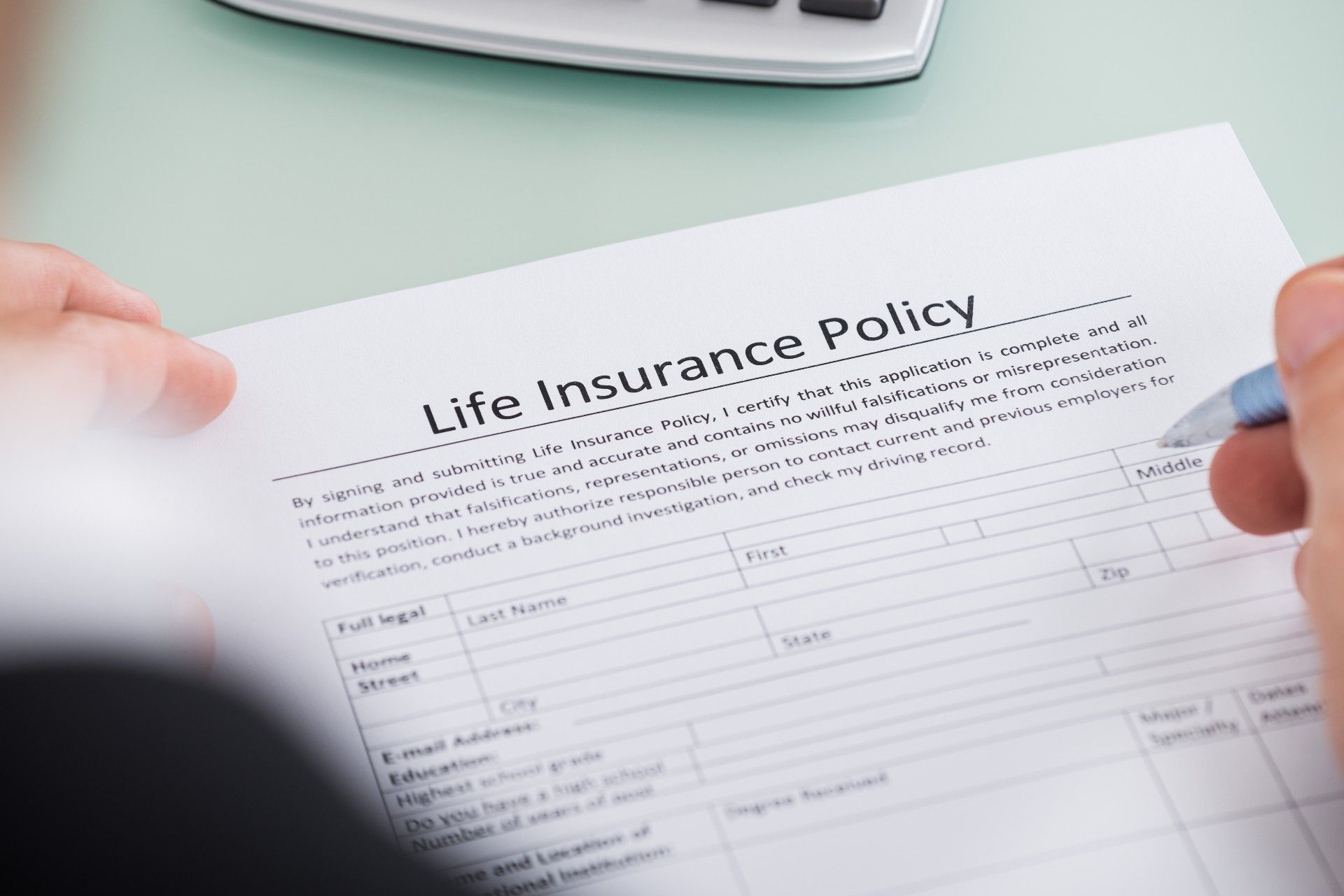 Closeup of a person's hand filing out life insurance policy paperwork - pacific life insurance company