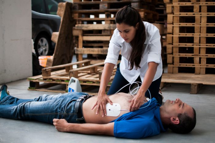 woman using defibrillator on fallen man