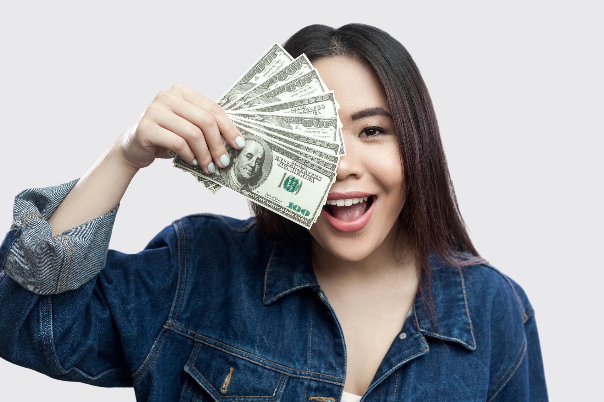 A happy Asian woman holds found out cash in front of half her face - class action settlement checks