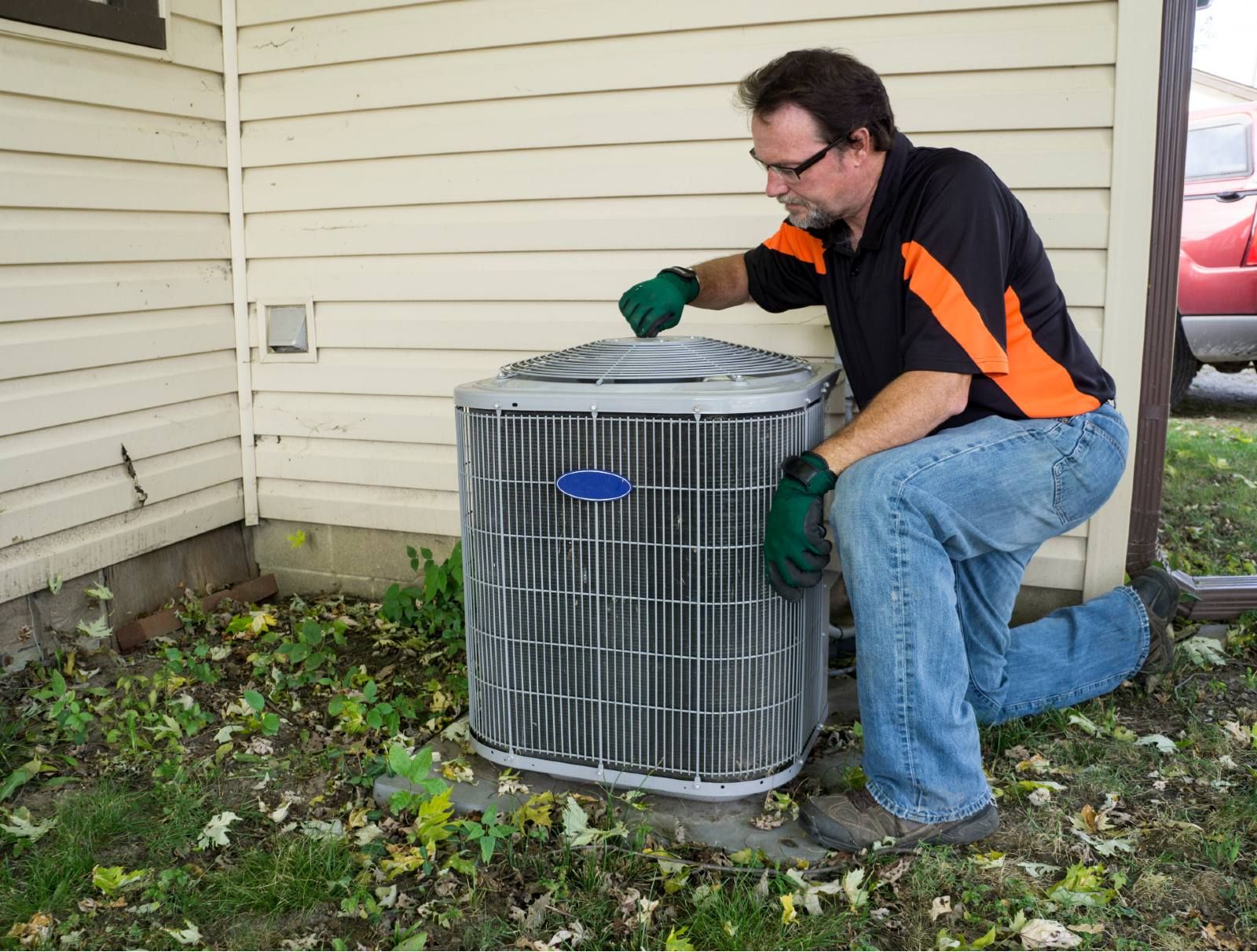 A repair technician works on an air-conditioning unit outside a house - landmark home warranty