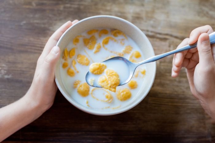 kellogg class action - Overhead shot of a person's left hand on a bowl of cereal, with a spoon of cereal in their right hand. - kellogg's cereal - kellogg cereals - 