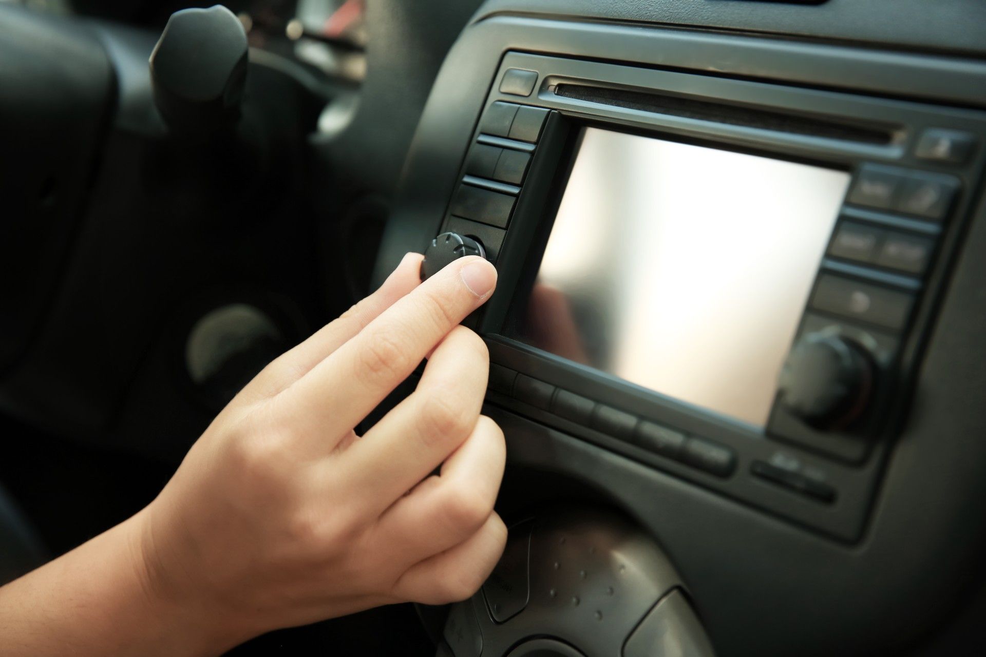 A driver's hand adjusts the volume on a car's infotainment system - GM