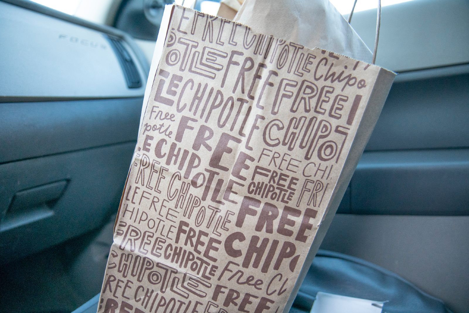 A Chipotle carryout bag sits on the passenger seat of a vehicle - delivery fees