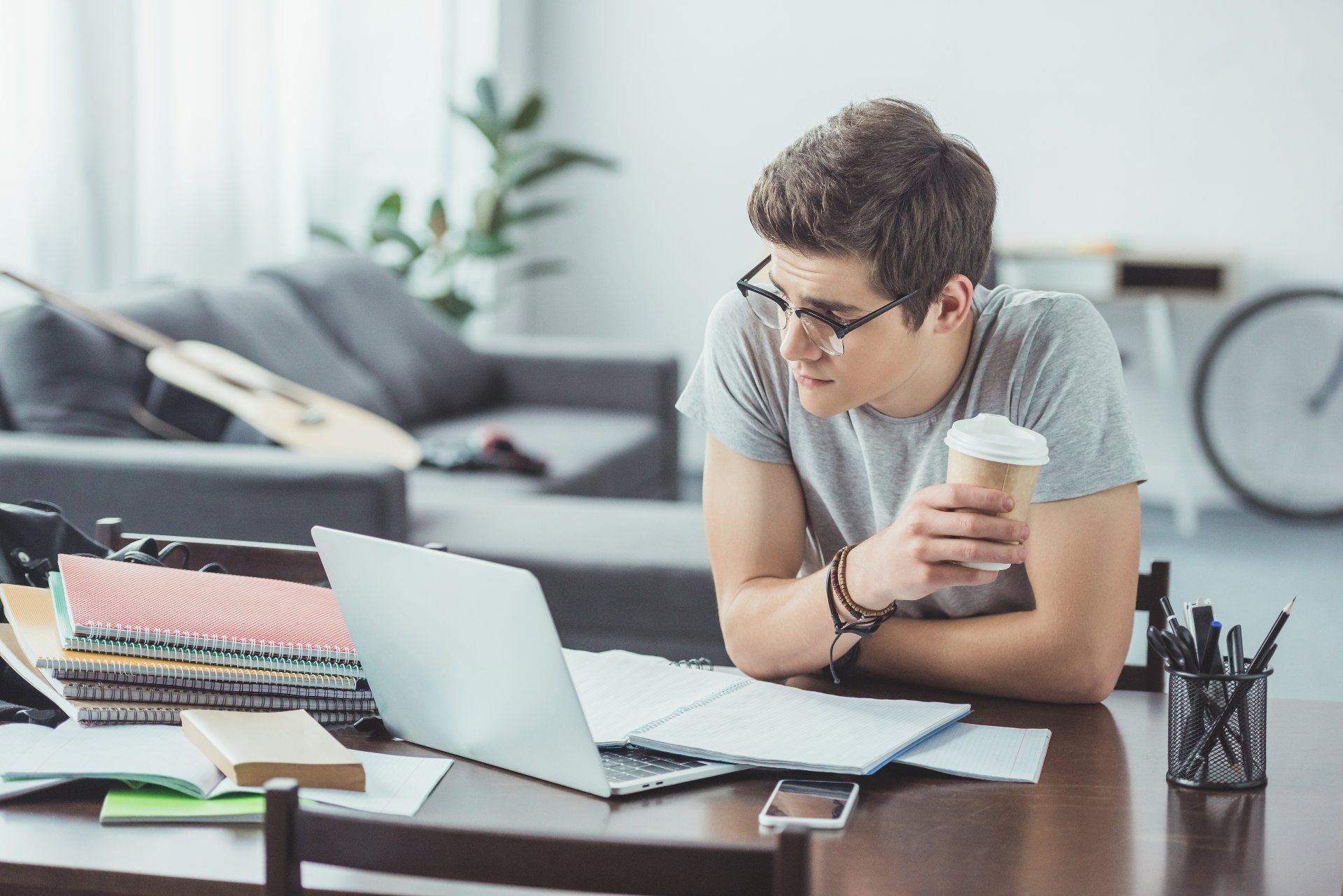 Male student with coffee and glasses studies on his laptop at home - tuition refund