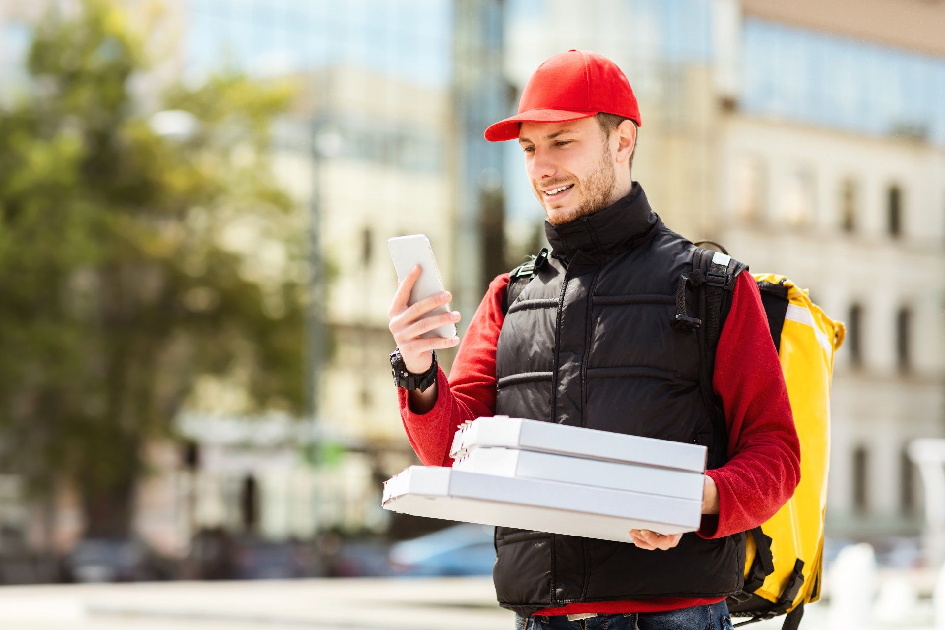 A food delivery man looks at a smartphone while carrying pizza boxes - delivery fees