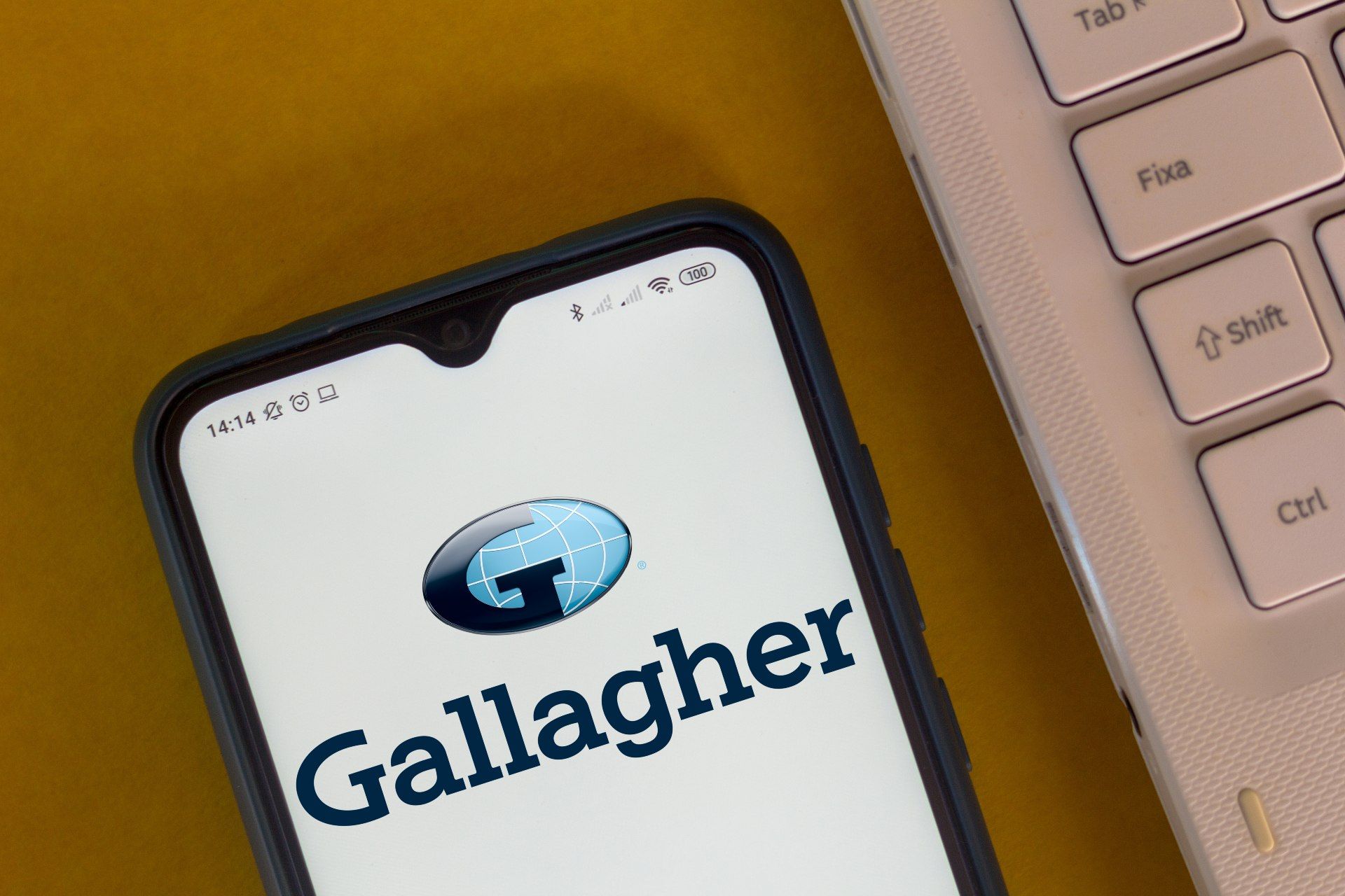 The Arthur J. Gallagher logo is seen on the screen of a smartphone lying next to a computer keyboard