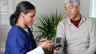 A home health care worker in dark blue scrubs takes an elderly man's blood pressure - humana home health