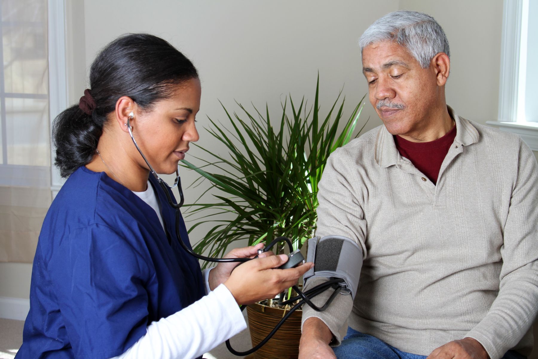 A home health care worker in dark blue scrubs takes an elderly man's blood pressure - humana