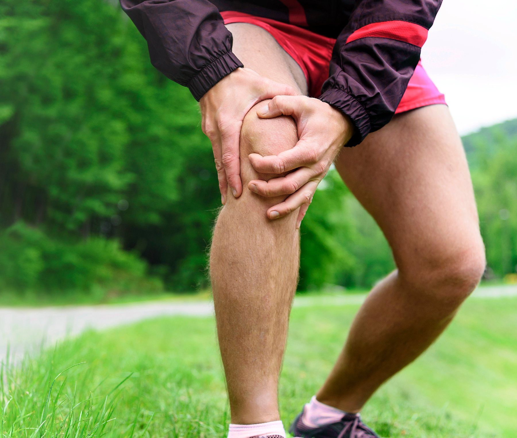 A runner grabs his knee in pain as he stands in the grass - spring valley glucosamine