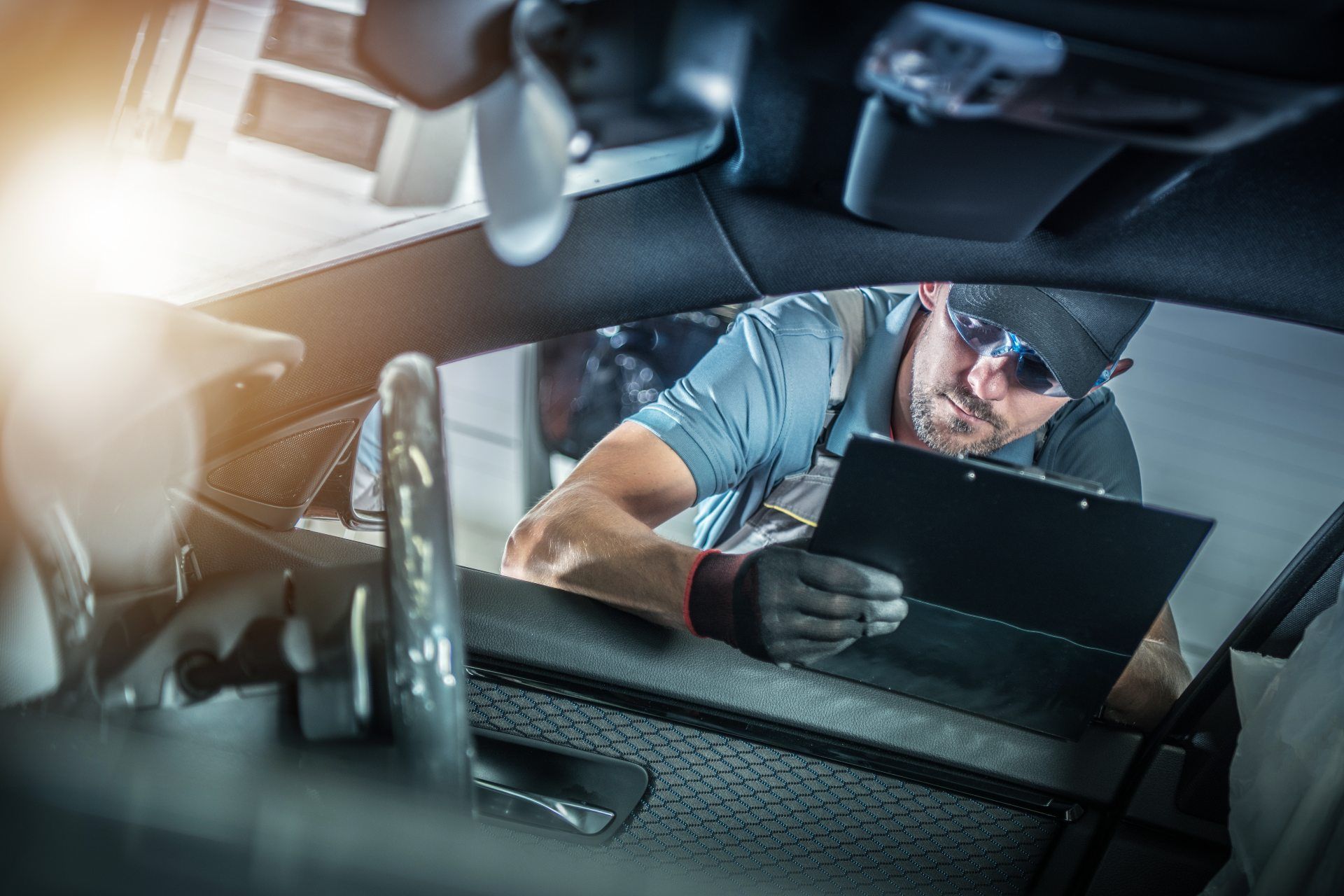 A car service technician holding a clipboard looks in the passenger-side front window of a vehicle - auto recalls