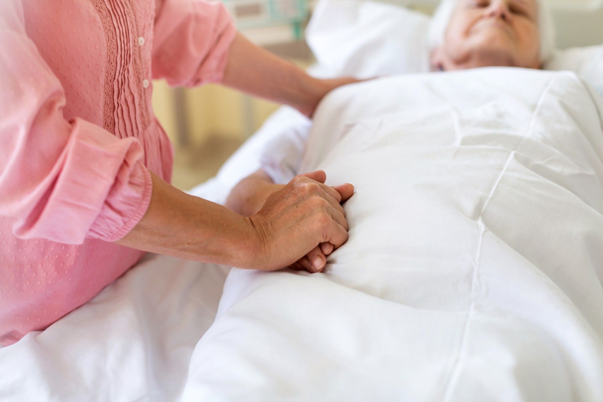 A woman holds the hand of a patient lying in a nursing home bed - nursing home deaths